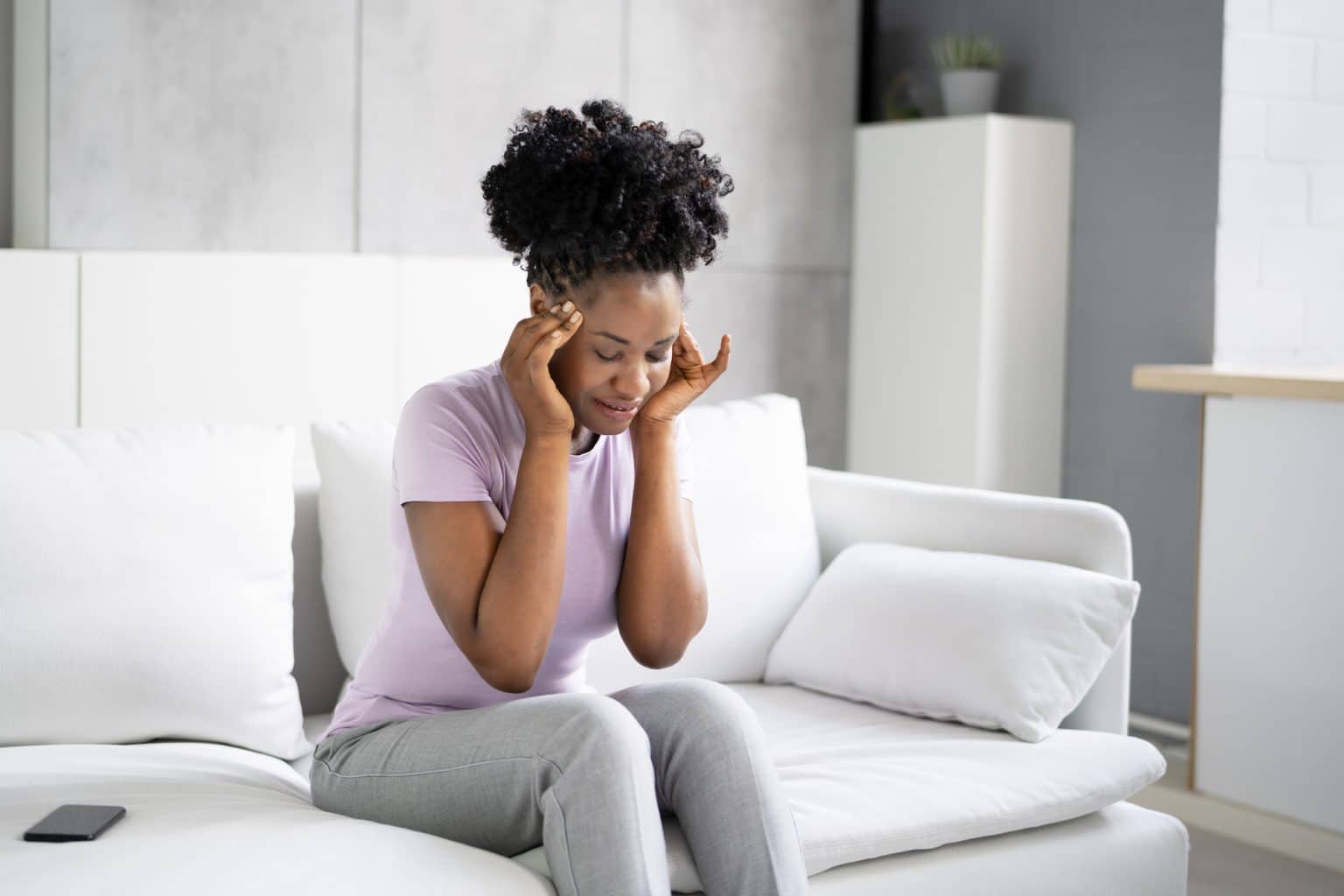 Woman on the couch holding her temples lightly with her hands while experiencing a bppv spell